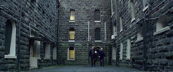 Movie still from “Hunt for the Wilderpeople” (2016), directed by Taika Waititi – Two men are standing in front of a brick building; Extreme Wide shot, Low angle