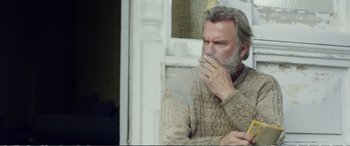 Movie still from “Hunt for the Wilderpeople” (2016), directed by Taika Waititi – An older man smoking a cigarette while wearing a sweater; Medium shot, Low angle