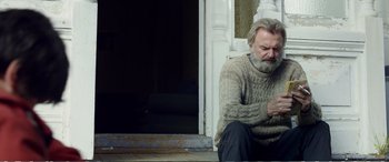 Movie still from “Hunt for the Wilderpeople” (2016), directed by Taika Waititi – An older man sitting on the steps of a house; Medium shot, Low angle