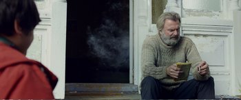 Movie still from “Hunt for the Wilderpeople” (2016), directed by Taika Waititi – An older man sitting on the steps of a building; Medium shot, Low angle