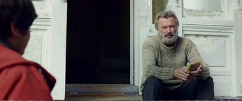 Movie still from “Hunt for the Wilderpeople” (2016), directed by Taika Waititi – A man sitting on the steps of a building; Medium shot, Low angle