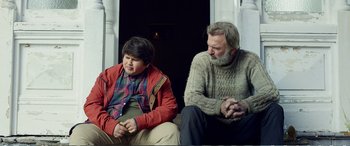 Movie still from “Hunt for the Wilderpeople” (2016), directed by Taika Waititi – A man and a boy sitting next to each other on a porch; Medium shot, Over the shoulder angle