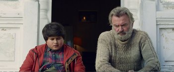 Movie still from “Hunt for the Wilderpeople” (2016), directed by Taika Waititi – A man sitting next to a boy in a sweater; Medium shot, Over the shoulder angle