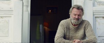 Movie still from “Hunt for the Wilderpeople” (2016), directed by Taika Waititi – An older man sitting in front of a refrigerator; Medium shot, Over the shoulder angle