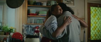 Movie still from “Hustle” (2022), directed by Jeremiah Zagar – Two women hugging in a kitchen with a cake on the counter; Medium shot, Over the shoulder angle
