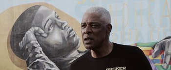 Movie still from “Hustle” (2022), directed by Jeremiah Zagar – An older black man with gray hair standing in front of a mural; Close Up shot, Low angle