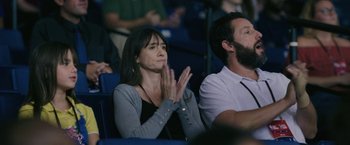 Movie still from “Hustle” (2022), directed by Jeremiah Zagar – A woman claps her hands while sitting next to a man; Medium shot, High angle