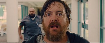 Movie still from “I Care a Lot” (2020), directed by J Blakeson – A man with long hair and a goatee stares at the camera; Close Up shot, Low angle