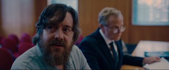 Movie still from “I Care a Lot” (2020), directed by J Blakeson – A man with a goatee sitting next to another man in a suit; Close Up shot, Over the shoulder angle