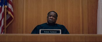 Movie still from “I Care a Lot” (2020), directed by J Blakeson – A judge sitting in front of a wooden wall; Close Up shot, Low angle