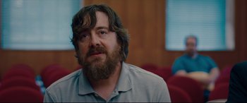 Movie still from “I Care a Lot” (2020), directed by J Blakeson – A man with a beard is sitting in front of a red couch; Close Up shot, Over the shoulder angle