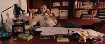 Movie still from “I Care a Lot” (2020), directed by J Blakeson – A man sitting at a desk talking on a phone; Medium shot, High angle