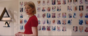 Movie still from “I Care a Lot” (2020), directed by J Blakeson – A woman standing in front of a bunch of pictures; Medium shot, Over the shoulder angle