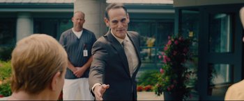 Movie still from “I Care a Lot” (2020), directed by J Blakeson – A man in a suit holding out his hand; Medium shot, Over the shoulder angle