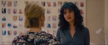 Movie still from “I Care a Lot” (2020), directed by J Blakeson – Two women are talking in front of a wall of pictures; Close Up shot, Over the shoulder angle
