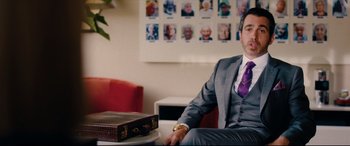Movie still from “I Care a Lot” (2020), directed by J Blakeson – A man in a suit sitting on a chair in a room; Medium shot, Over the shoulder angle