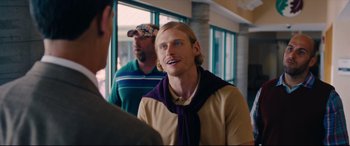 Movie still from “I Care a Lot” (2020), directed by J Blakeson – A man with a purple scarf is talking to two other men; Close Up shot, Over the shoulder angle