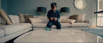 Movie still from “I Care a Lot” (2020), directed by J Blakeson – A man sitting on a couch in a living room; Wide shot, High angle