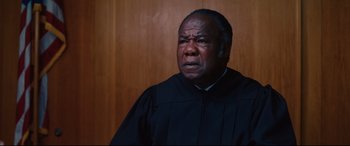 Movie still from “I Care a Lot” (2020), directed by J Blakeson – A man in a black robe is looking at the camera; Close Up shot, Low angle