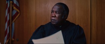Movie still from “I Care a Lot” (2020), directed by J Blakeson – An older man wearing a black robe is holding a paper; Close Up shot, Low angle