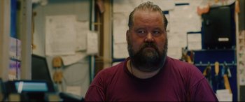 Movie still from “I Care a Lot” (2020), directed by J Blakeson – A man with a goatee and beard wearing a red shirt; Close Up shot, Over the shoulder angle