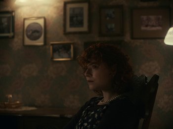 Movie still from “I'm Thinking of Ending Things” (2020), directed by Charlie Kaufman – A woman sitting in a chair in front of pictures; Medium shot, Over the shoulder angle