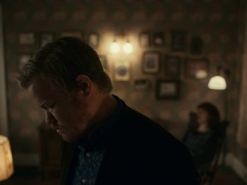 Movie still from “I'm Thinking of Ending Things” (2020), directed by Charlie Kaufman – A man standing in front of a woman in a dark room; Medium shot, Over the shoulder angle