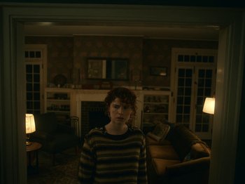 Movie still from “I'm Thinking of Ending Things” (2020), directed by Charlie Kaufman – A person standing in a living room in the dark; Medium shot, Low angle