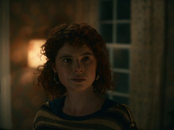 Movie still from “I'm Thinking of Ending Things” (2020), directed by Charlie Kaufman – A woman with curly red hair standing in front of a window at night; Close Up shot, Low angle