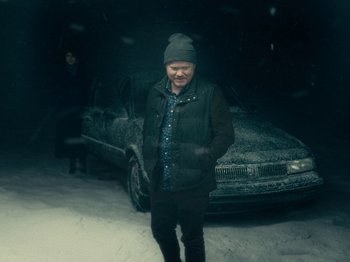 Movie still from “I'm Thinking of Ending Things” (2020), directed by Charlie Kaufman – A man standing in front of a car in the snow; Wide shot, High angle