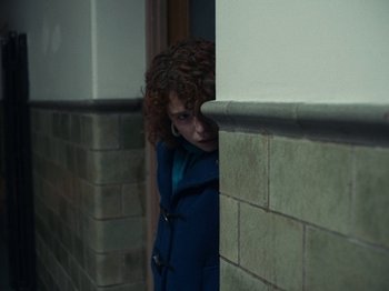Movie still from “I'm Thinking of Ending Things” (2020), directed by Charlie Kaufman – A woman in a blue coat leaning against a brick wall; Medium shot, High angle