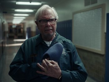 Movie still from “I'm Thinking of Ending Things” (2020), directed by Charlie Kaufman – An older man holding a blue bag in a hallway; Close Up shot, Low angle