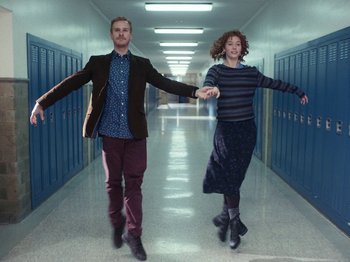 Movie still from “I'm Thinking of Ending Things” (2020), directed by Charlie Kaufman – A man and a woman holding hands while walking down a hall way; Wide shot, Low angle