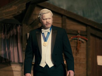Movie still from “I'm Thinking of Ending Things” (2020), directed by Charlie Kaufman – A man in a suit and tie wearing a gold medal; Medium shot, High angle