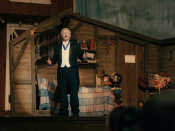 Movie still from “I'm Thinking of Ending Things” (2020), directed by Charlie Kaufman – A man standing on a stage in front of a barn; Wide shot, Low angle