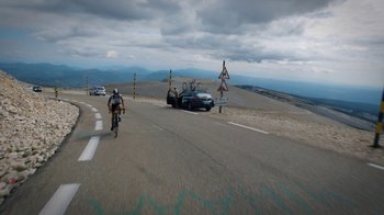 Movie still from “Icarus” (2017), directed by Bryan Fogel – A man riding a bike down the side of a road next to cars; Extreme Wide shot, High angle