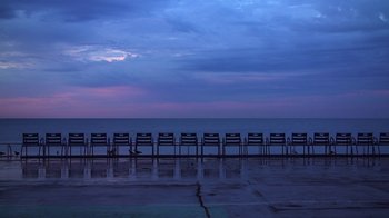 Movie still from “Icarus” (2017), directed by Bryan Fogel – A row of chairs sitting in front of the ocean at dusk; Extreme Wide shot, High angle