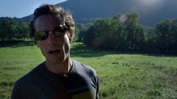 Movie still from “Icarus” (2017), directed by Bryan Fogel – A man in sunglasses standing in a grassy field; Close Up shot, Low angle