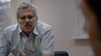 Movie still from “Icarus” (2017), directed by Bryan Fogel – An older man sitting at a desk looking at the camera; Close Up shot, Over the shoulder angle