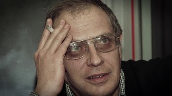 Movie still from “Icarus” (2017), directed by Bryan Fogel – A person wearing glasses and holding a cigarette; Close Up shot, Low angle