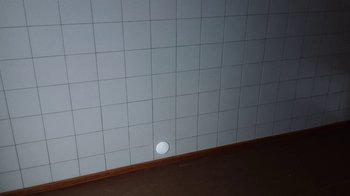 Movie still from “Icarus” (2017), directed by Bryan Fogel – A white tile wall in a room with a white tile floor; Extreme Wide shot, High angle