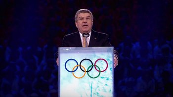 Movie still from “Icarus” (2017), directed by Bryan Fogel – A man standing at a podium in front of an image of olympic rings; Medium shot, Low angle