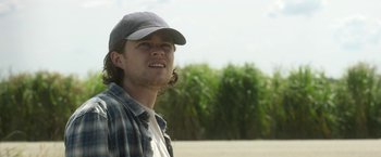 Movie still from “In the Tall Grass” (2019), directed by Vincenzo Natali – A young man wearing a hat and a plaid shirt; Close Up shot, Low angle