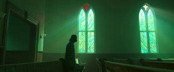 Movie still from “In the Tall Grass” (2019), directed by Vincenzo Natali – A man standing in front of a stained - glass window; Medium shot, Low angle