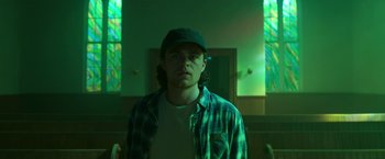 Movie still from “In the Tall Grass” (2019), directed by Vincenzo Natali – A man standing in front of a stained glass window; Medium shot, Low angle