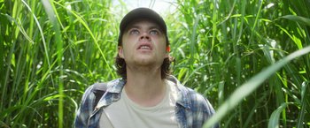 Movie still from “In the Tall Grass” (2019), directed by Vincenzo Natali – A young man in a baseball cap looking up at the sky; Close Up shot, Low angle