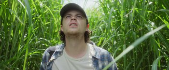 Movie still from “In the Tall Grass” (2019), directed by Vincenzo Natali – A young man in a baseball cap looking up at the sky; Close Up shot, Low angle