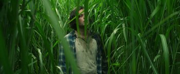 Movie still from “In the Tall Grass” (2019), directed by Vincenzo Natali – A man standing in tall green grass looking at the camera; Medium shot, Low angle