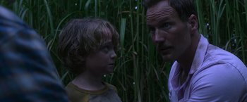 Movie still from “In the Tall Grass” (2019), directed by Vincenzo Natali – A man and a boy standing next to each other in front of tall grass; Close Up shot, Over the shoulder angle