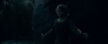 Movie still from “In the Tall Grass” (2019), directed by Vincenzo Natali – A young boy standing in the dark with his arms outstreched; Medium shot, Low angle